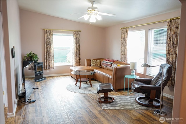 living area featuring a ceiling fan, a wood stove, wood finished floors, and a wealth of natural light