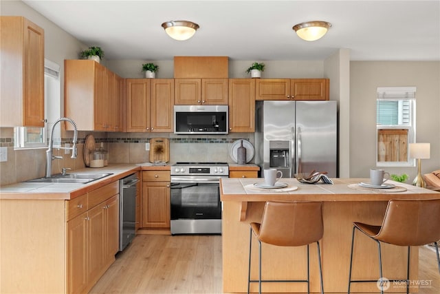 kitchen with tile countertops, appliances with stainless steel finishes, a breakfast bar area, and a sink