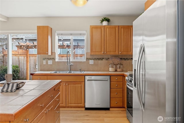 kitchen with tile countertops, a sink, stainless steel appliances, light wood-style floors, and backsplash