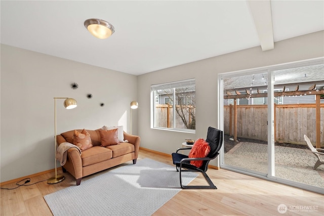 living room featuring beamed ceiling, baseboards, and light wood-style flooring