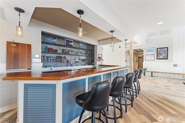 bar featuring visible vents, a bar, a wainscoted wall, and wood finished floors