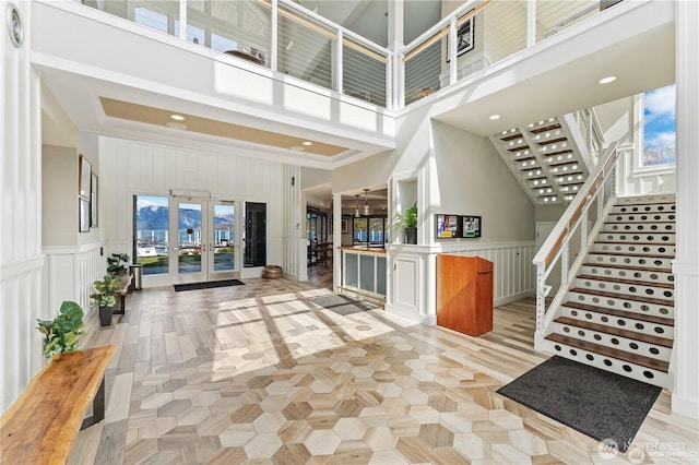 foyer featuring stairway, wainscoting, french doors, a towering ceiling, and a decorative wall