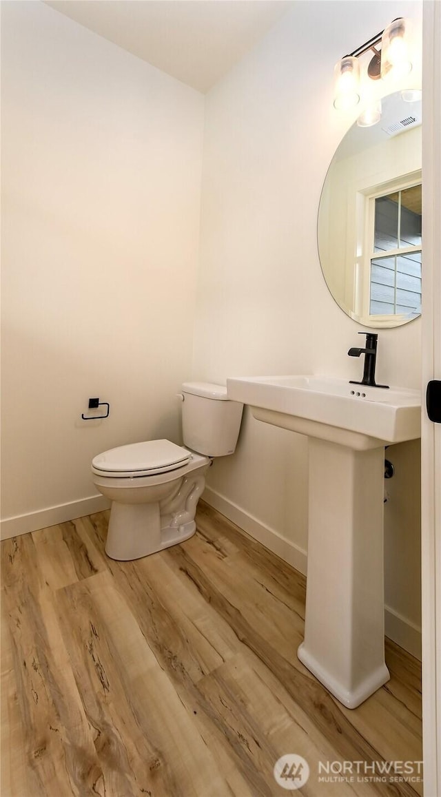 half bath featuring visible vents, baseboards, toilet, and wood finished floors