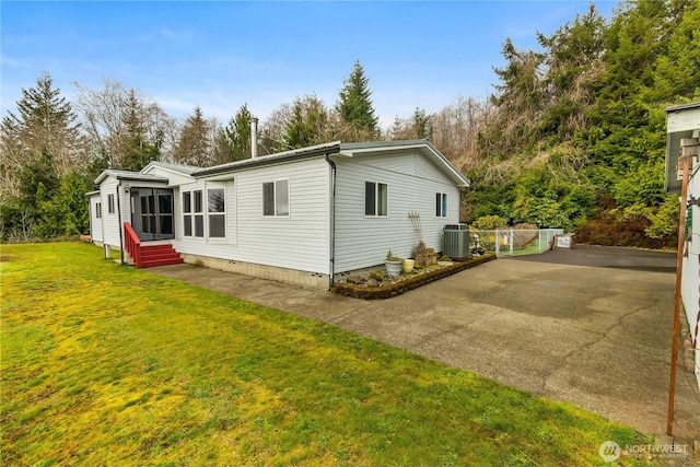 back of house featuring central air condition unit, entry steps, driveway, and a yard