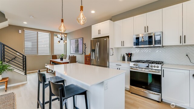 kitchen with stainless steel appliances, white cabinetry, a kitchen island, and light countertops