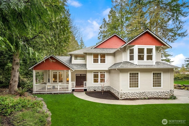 rear view of house featuring covered porch, a shingled roof, and a yard