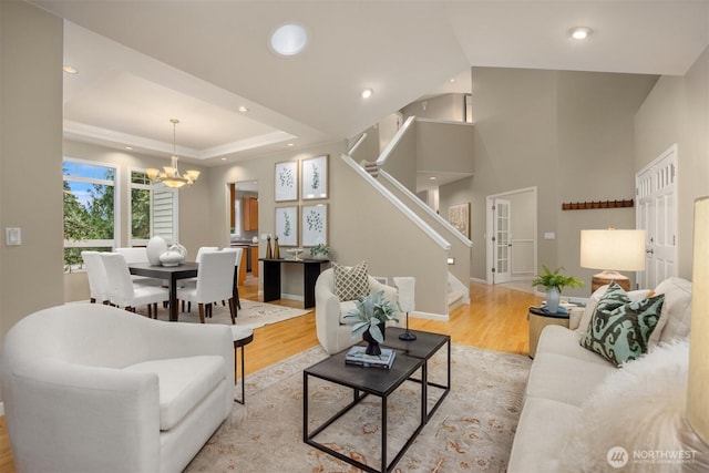 living area with stairway, light wood-type flooring, a tray ceiling, recessed lighting, and an inviting chandelier