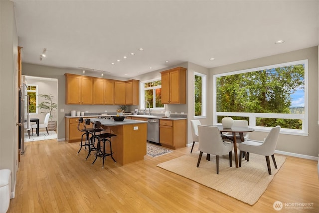 kitchen with light wood finished floors, a kitchen island, a breakfast bar area, fridge, and stainless steel dishwasher