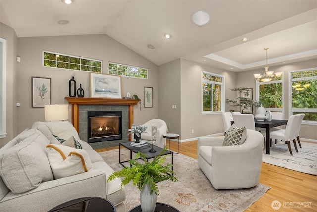 living room featuring a notable chandelier, lofted ceiling, light wood-style flooring, a tiled fireplace, and baseboards