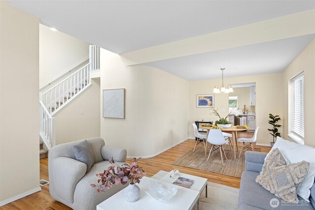 living room featuring light wood finished floors, a chandelier, stairs, and baseboards