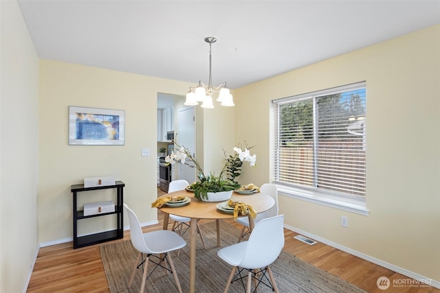 dining area with light wood-style flooring, a notable chandelier, visible vents, and baseboards