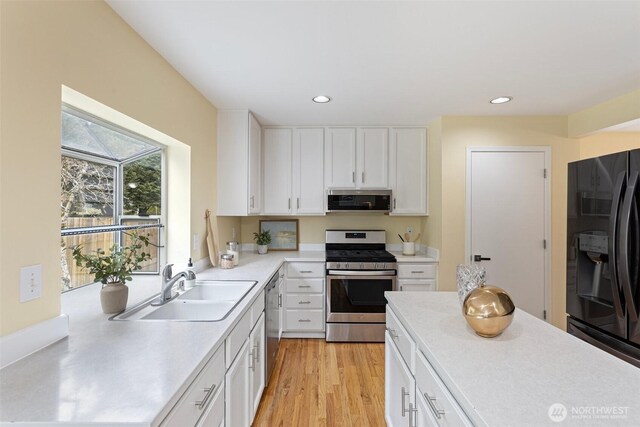 kitchen featuring light countertops, appliances with stainless steel finishes, exhaust hood, white cabinetry, and a sink