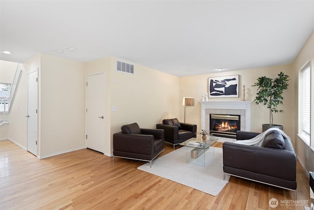 living room with a fireplace, light wood-style floors, visible vents, and baseboards