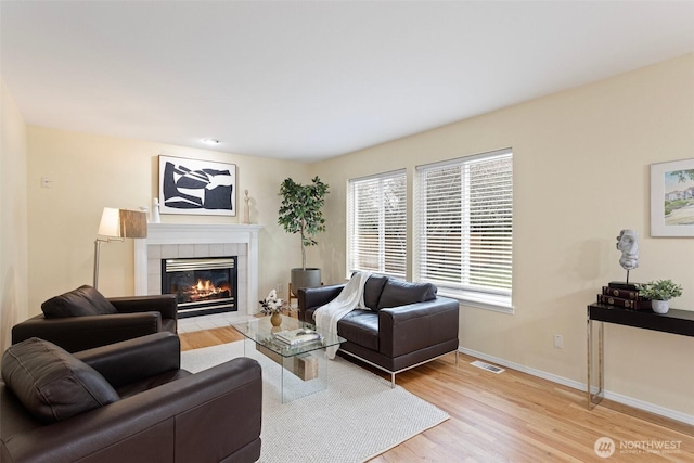 living room featuring visible vents, baseboards, a tile fireplace, and light wood finished floors