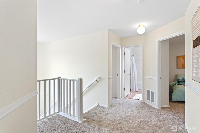 hallway with baseboards, visible vents, an upstairs landing, and carpet floors