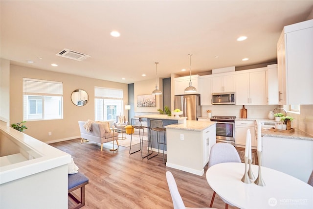 kitchen with backsplash, a kitchen island, stainless steel appliances, a breakfast bar area, and light wood finished floors