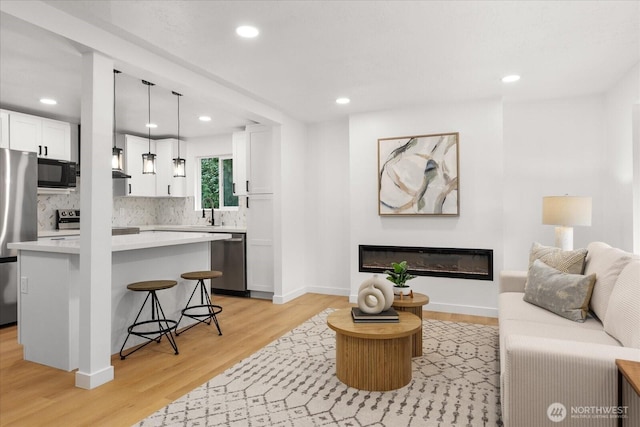 living room with a glass covered fireplace, recessed lighting, baseboards, and light wood finished floors