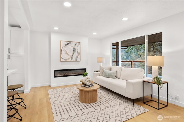 living room with a glass covered fireplace, recessed lighting, light wood-type flooring, and baseboards