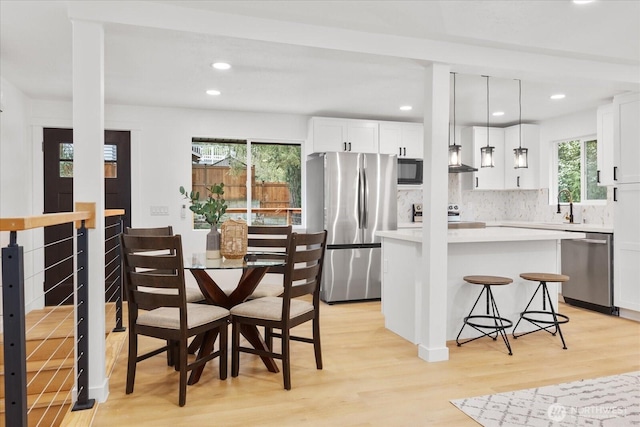 kitchen with a breakfast bar area, stainless steel appliances, light countertops, light wood-style floors, and white cabinetry