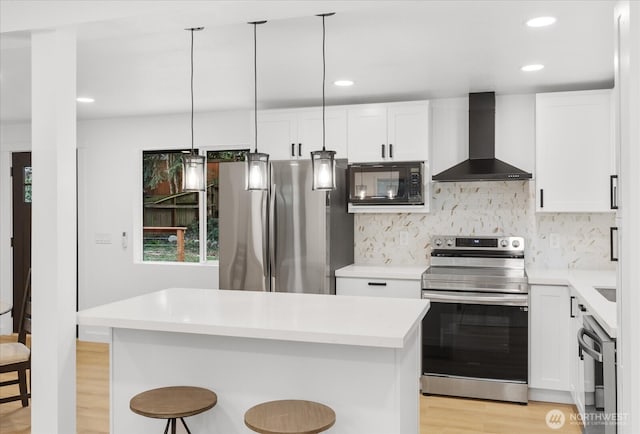 kitchen featuring a breakfast bar, light countertops, appliances with stainless steel finishes, white cabinets, and wall chimney exhaust hood