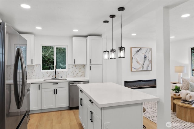 kitchen featuring a sink, a glass covered fireplace, stainless steel appliances, light wood finished floors, and light countertops