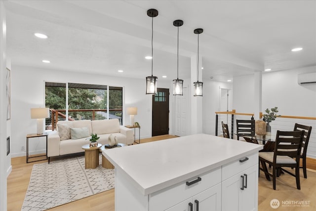 kitchen with decorative light fixtures, light countertops, a wall unit AC, light wood-style floors, and white cabinets