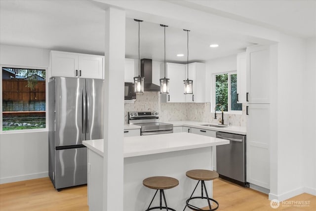 kitchen featuring a sink, stainless steel appliances, white cabinetry, wall chimney range hood, and tasteful backsplash