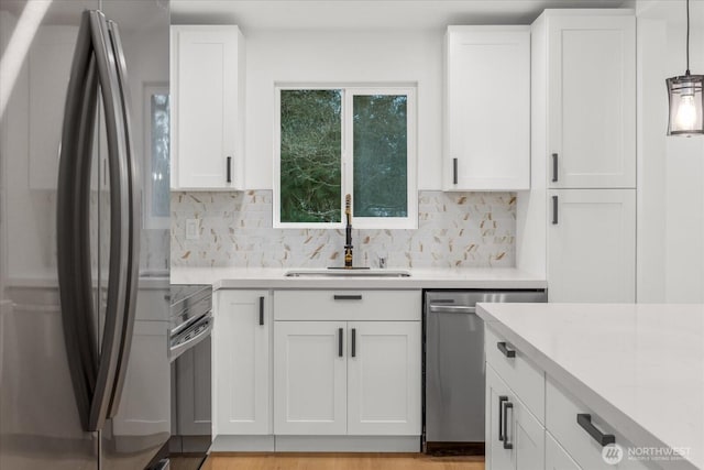 kitchen with white cabinetry, stainless steel appliances, light countertops, and a sink