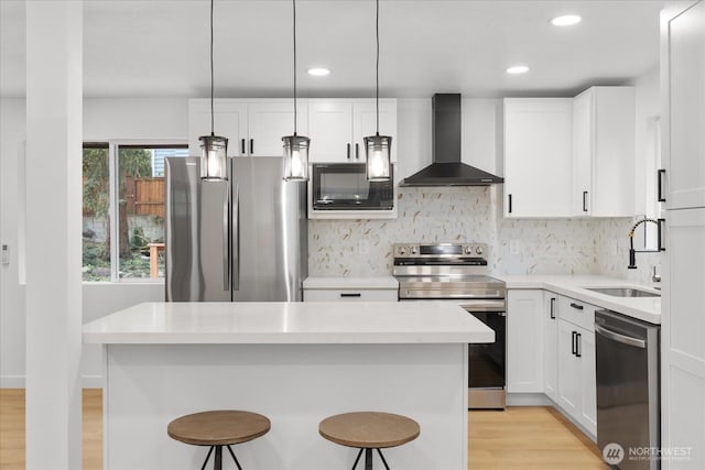 kitchen featuring a sink, white cabinets, appliances with stainless steel finishes, a kitchen breakfast bar, and wall chimney exhaust hood