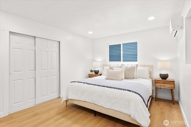 bedroom with a closet, recessed lighting, light wood-style flooring, and a wall mounted AC