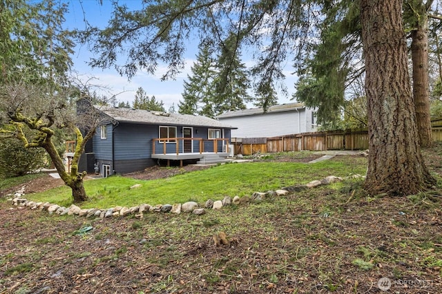 rear view of house with a deck, a yard, and fence