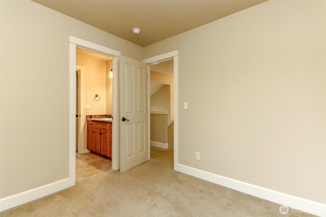 unfurnished bedroom featuring ensuite bath, light colored carpet, and baseboards