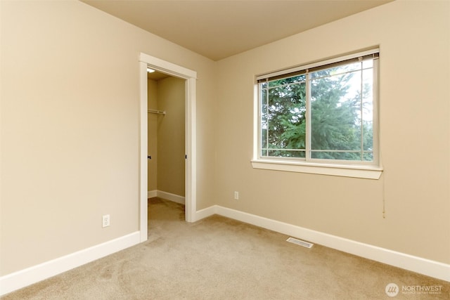 unfurnished bedroom with a spacious closet, visible vents, baseboards, light colored carpet, and a closet