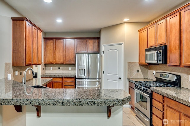 kitchen featuring a breakfast bar, a sink, stainless steel appliances, a peninsula, and light tile patterned flooring