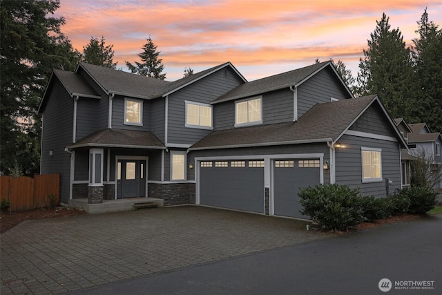 view of front of property with decorative driveway, stone siding, fence, an attached garage, and a shingled roof