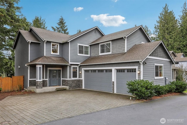 view of front of home featuring decorative driveway, stone siding, fence, a shingled roof, and a garage