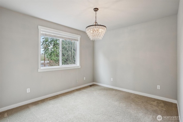 empty room featuring carpet, baseboards, and a chandelier