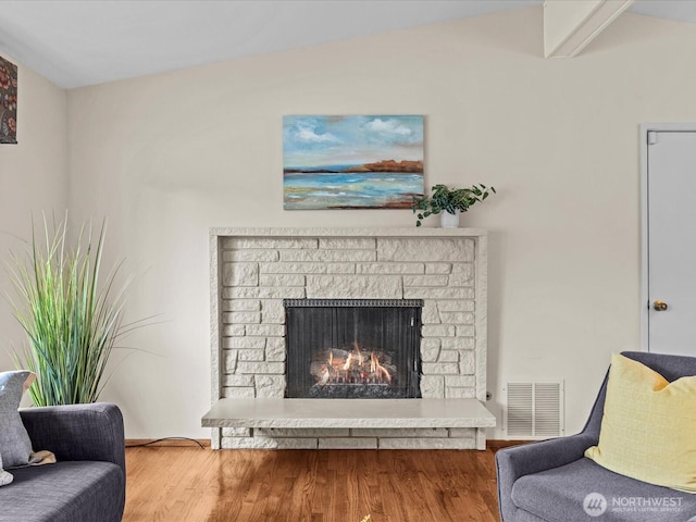 living room with visible vents, a warm lit fireplace, and wood finished floors