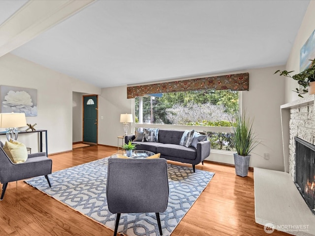 living area featuring a stone fireplace, baseboards, and wood finished floors