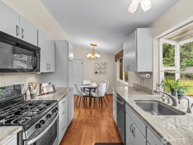 kitchen with a sink, wood finished floors, appliances with stainless steel finishes, a chandelier, and hanging light fixtures