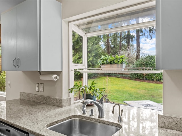 kitchen with a sink, light stone counters, stainless steel dishwasher, and a wealth of natural light