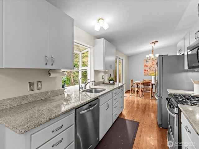 kitchen featuring light wood-style flooring, a sink, appliances with stainless steel finishes, white cabinets, and vaulted ceiling