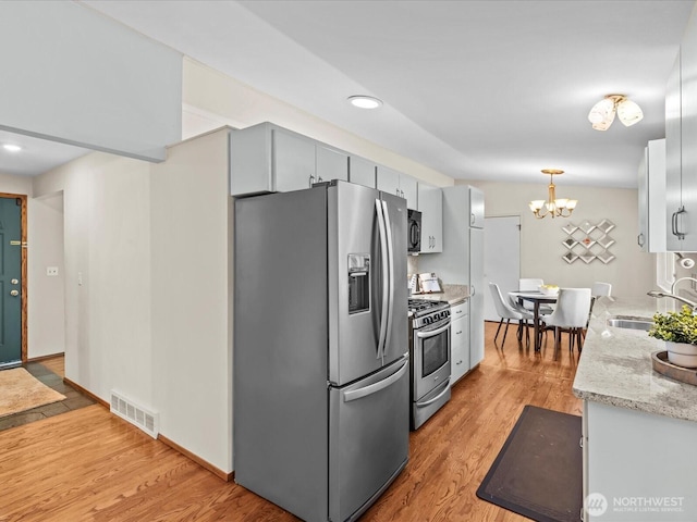 kitchen featuring visible vents, a sink, stainless steel appliances, a notable chandelier, and light wood-type flooring