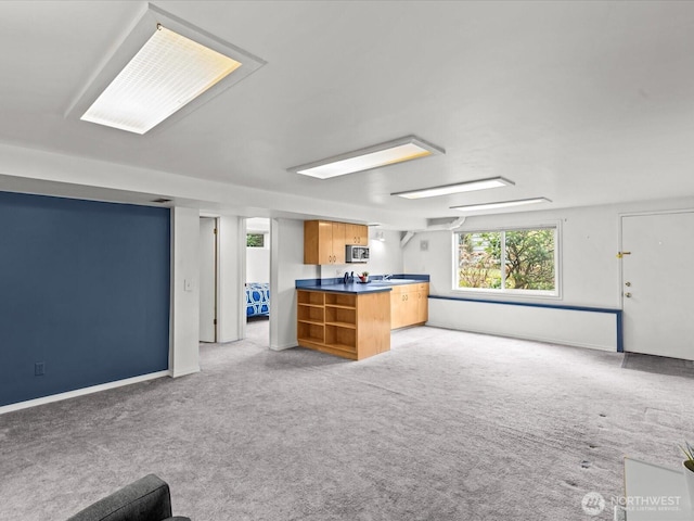 kitchen featuring stainless steel microwave, dark countertops, open floor plan, and light carpet