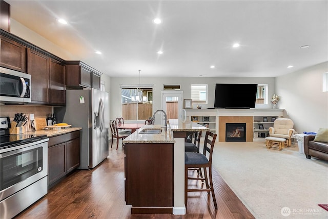 kitchen featuring a breakfast bar, a sink, stainless steel appliances, a fireplace, and dark brown cabinets