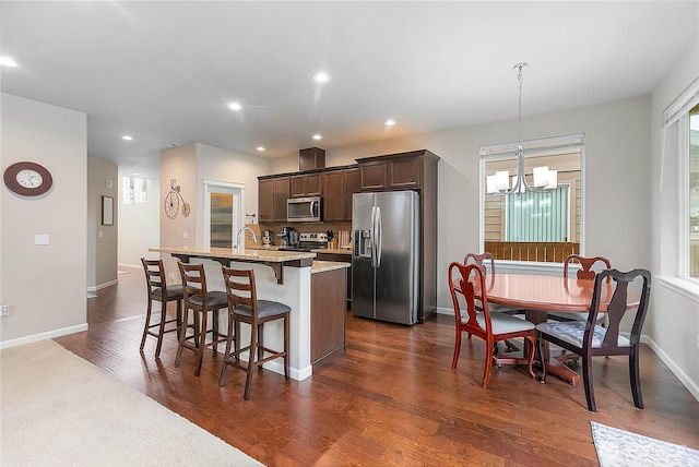 kitchen featuring a center island with sink, a breakfast bar, dark brown cabinetry, dark wood-type flooring, and appliances with stainless steel finishes