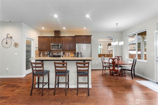 kitchen featuring dark wood-style floors, a notable chandelier, appliances with stainless steel finishes, and a breakfast bar area