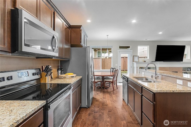 kitchen featuring light stone countertops, a sink, dark wood-type flooring, appliances with stainless steel finishes, and decorative light fixtures