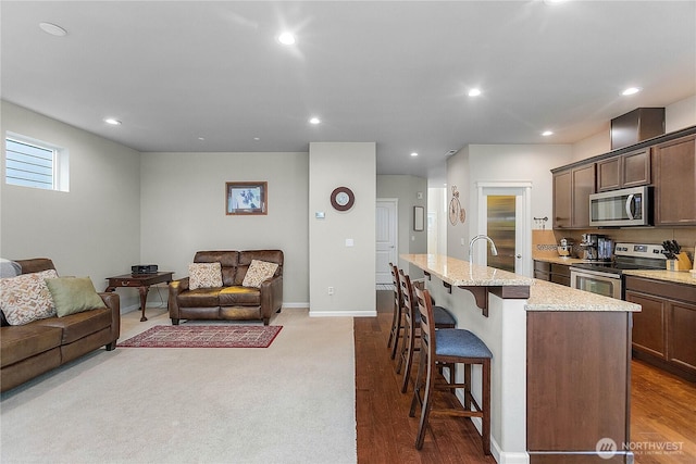 kitchen featuring recessed lighting, stainless steel appliances, a kitchen bar, and an island with sink