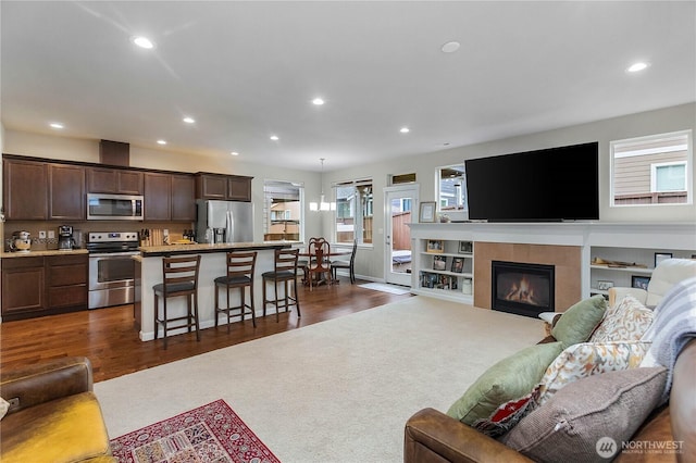 living area with recessed lighting, a tile fireplace, dark wood-type flooring, and dark colored carpet